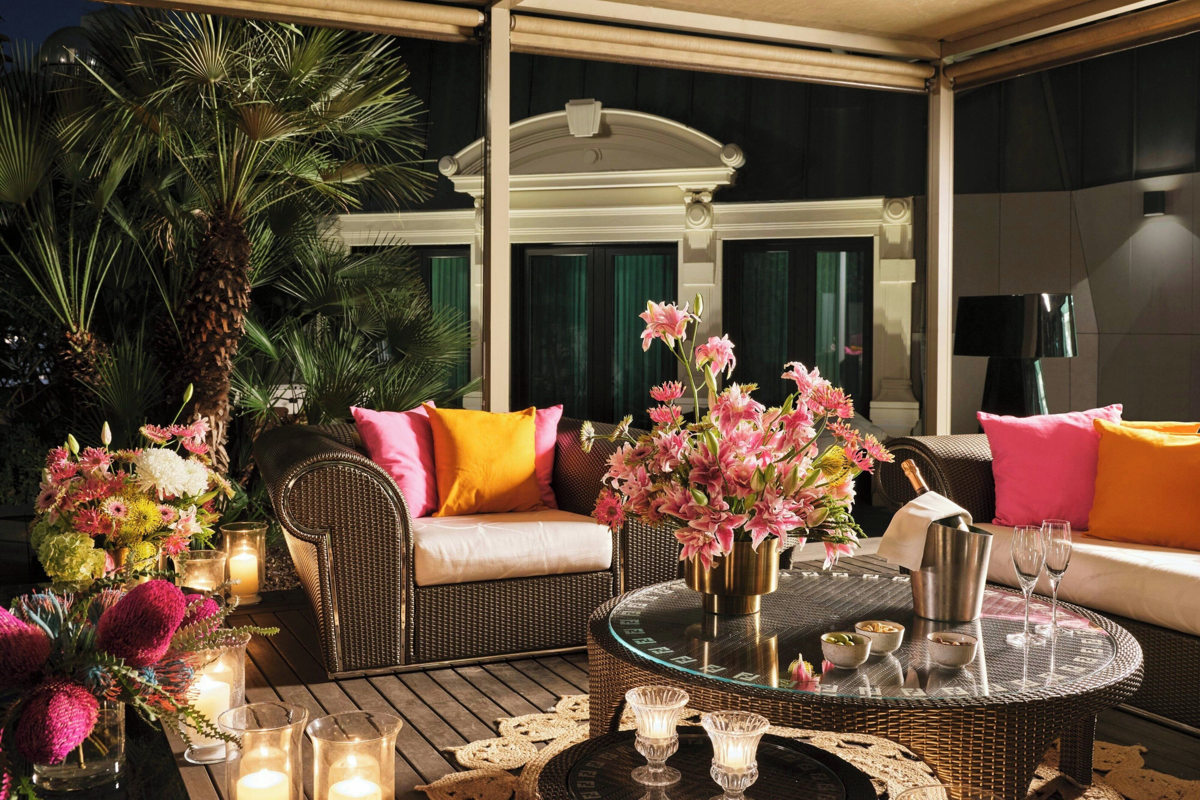 An outdoor seating area with wicker furniture, cushions, and floral arrangements.