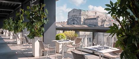 A rooftop terrace with outdoor seating, large potted plants, and a view of historic architecture.