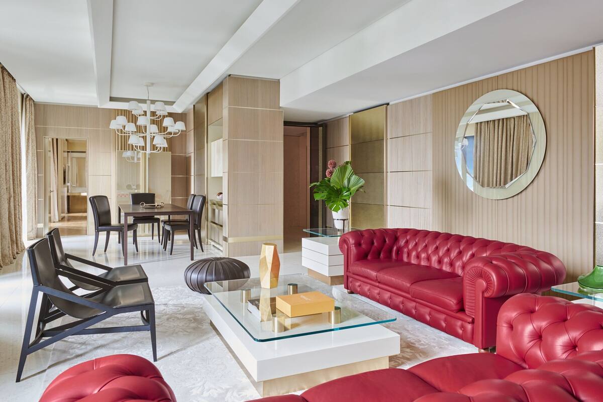 A modern living room with a red sofa, black chairs, a glass coffee table, and a dining area with a table and chairs.