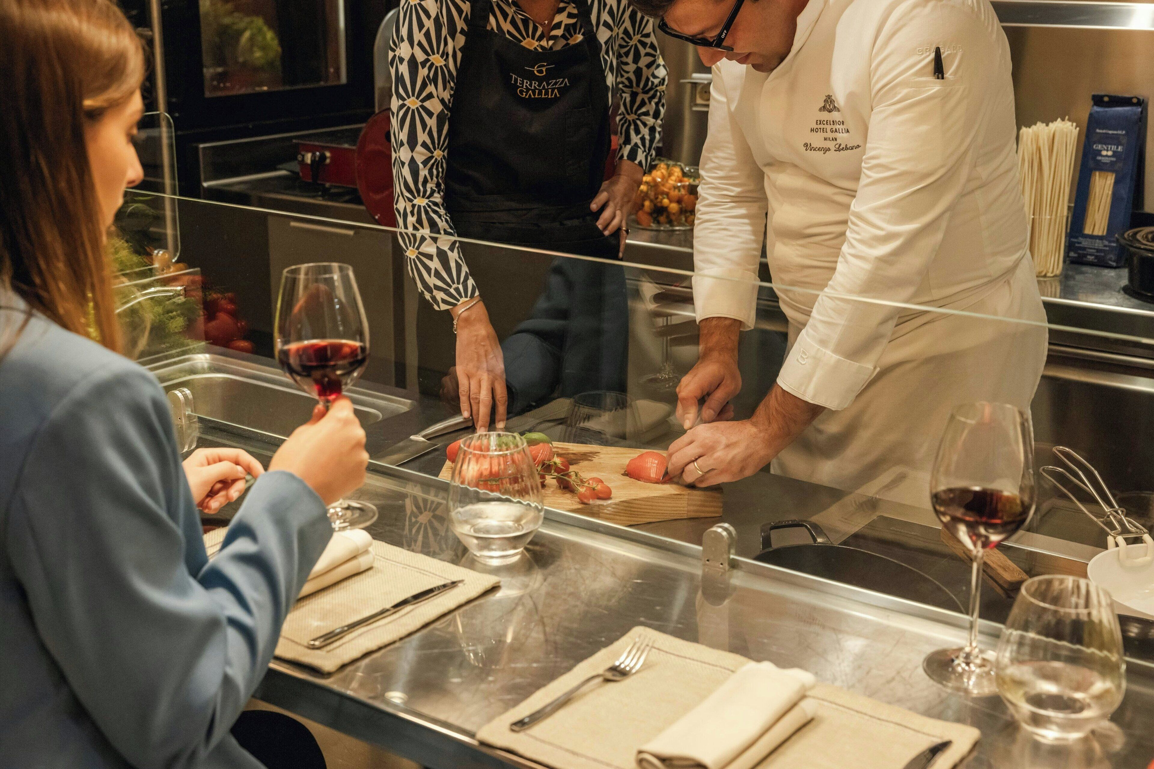 A chef preparing food at a counter with a customer and a server.