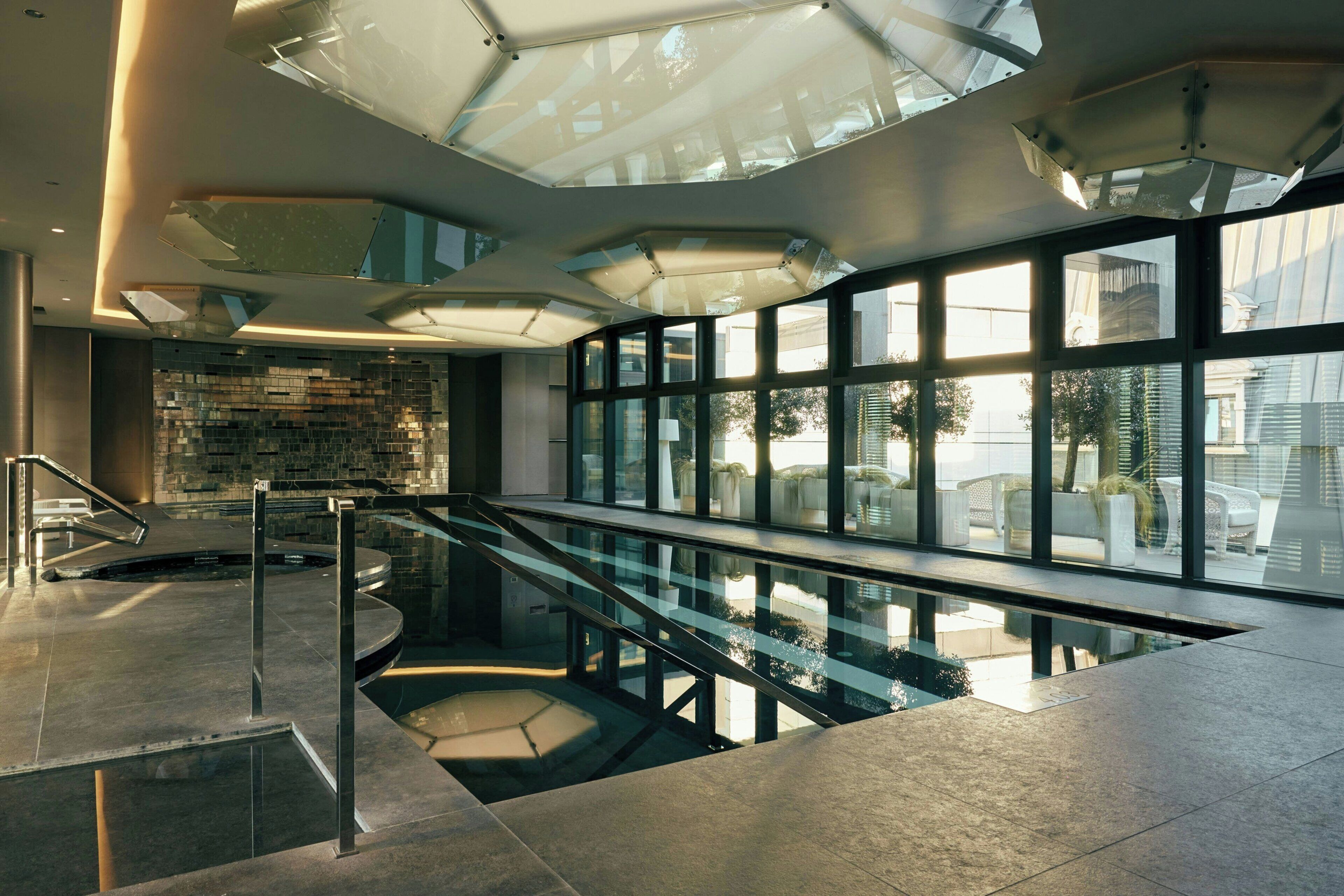 Un interior moderno con una piscina de fondo de cristal, barandales de metal y ventanas amplias con vistas al exterior.