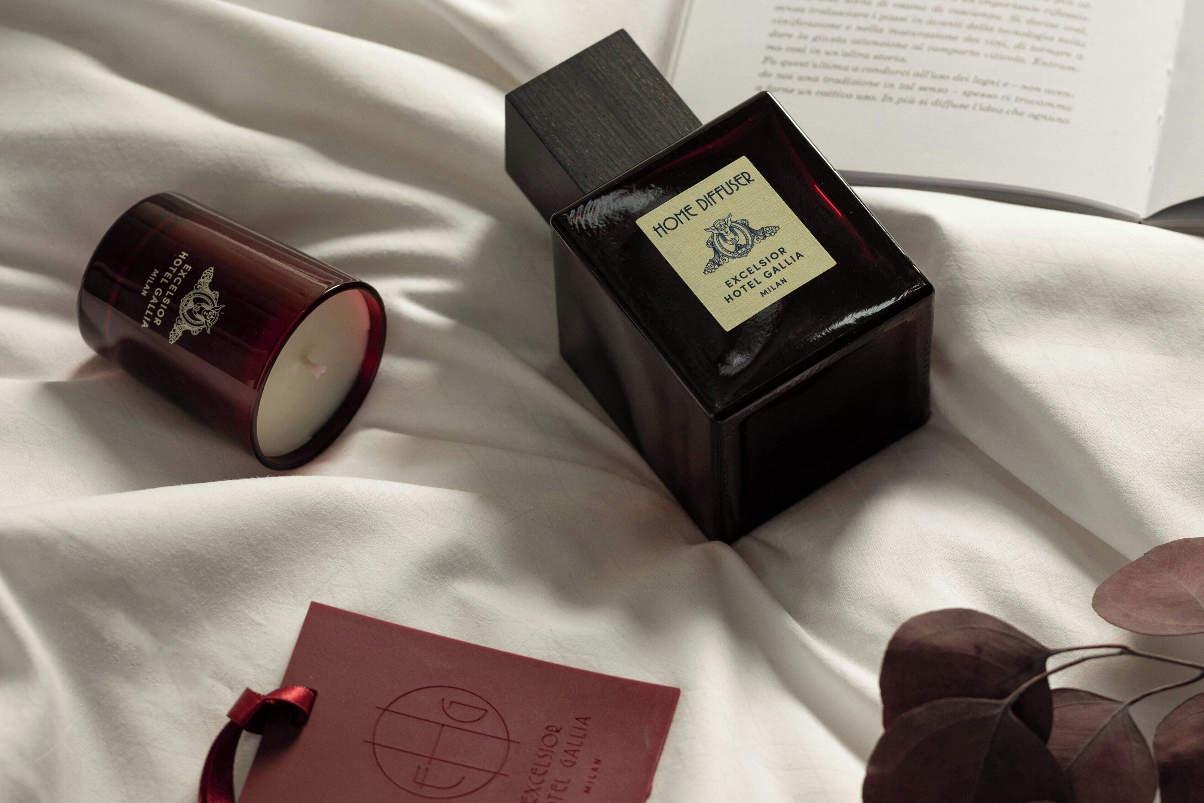 A candle, a bottle of Home Diffuser, and a tag on a white fabric surface.