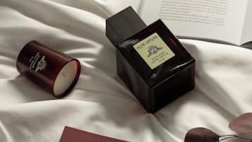Una candela, una bottiglia di Diffusore Ambiente e un'etichetta su una superficie in tessuto bianco.