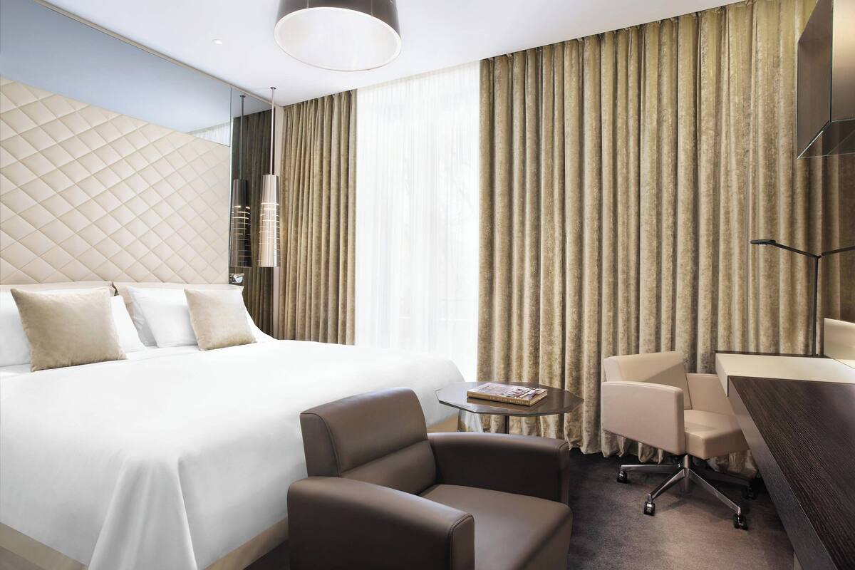 A hotel room with a large bed, a desk, a chair, and a small table.