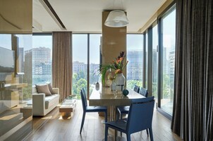 A modern living room with a glass partition, a sofa, a dining table with chairs, and a large window with curtains.