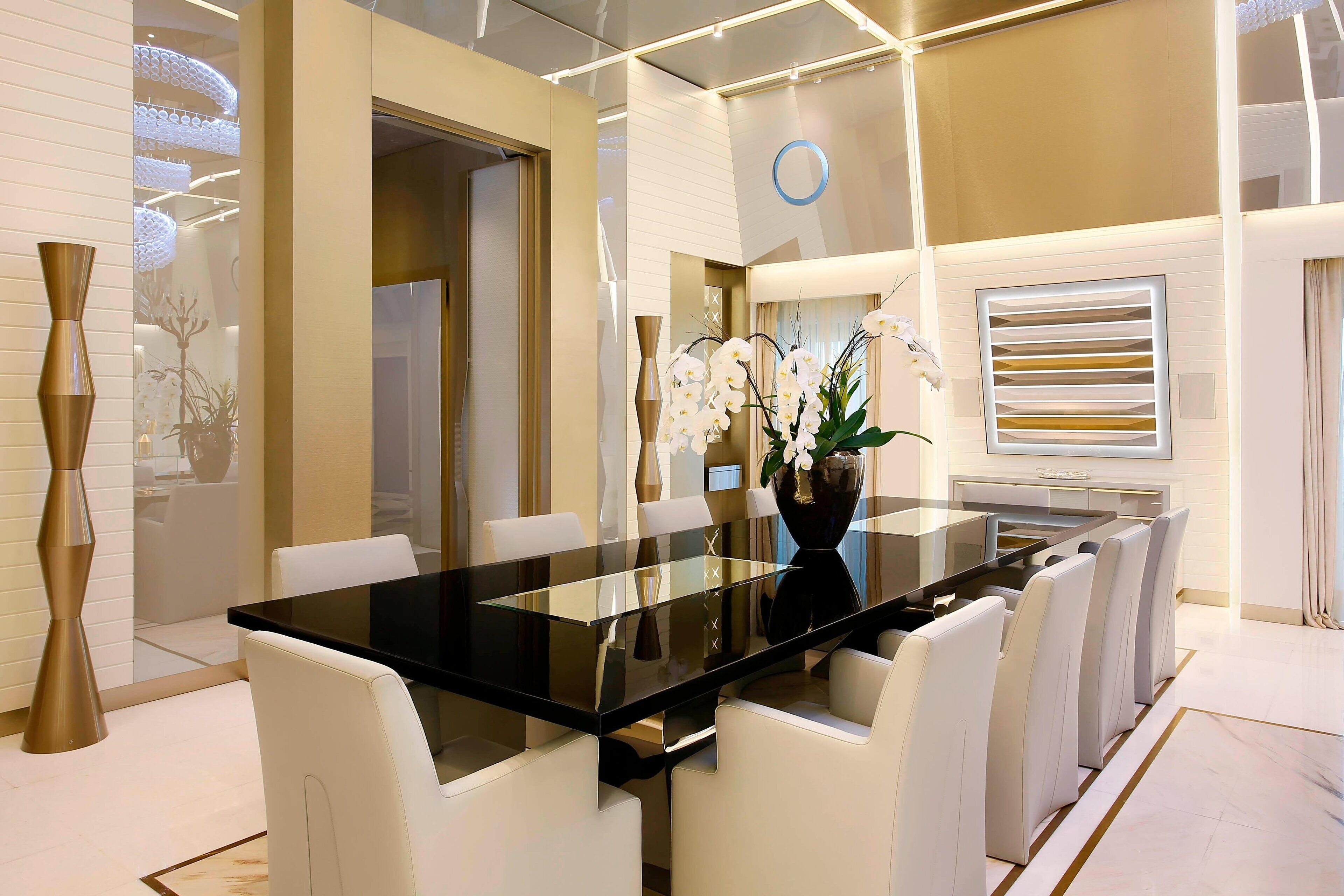 Un comedor moderno con una mesa de vidrio y sillas blancas, un jarrón con orquídeas y un panel decorativo en la pared.