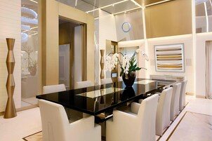Un comedor moderno con una mesa de vidrio y sillas blancas, un jarrón con orquídeas y un panel decorativo en la pared.