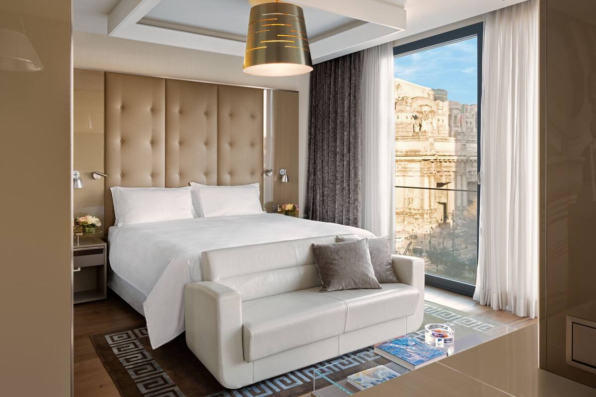 A modern bedroom with a large bed, a sofa, and a view of a historic building.