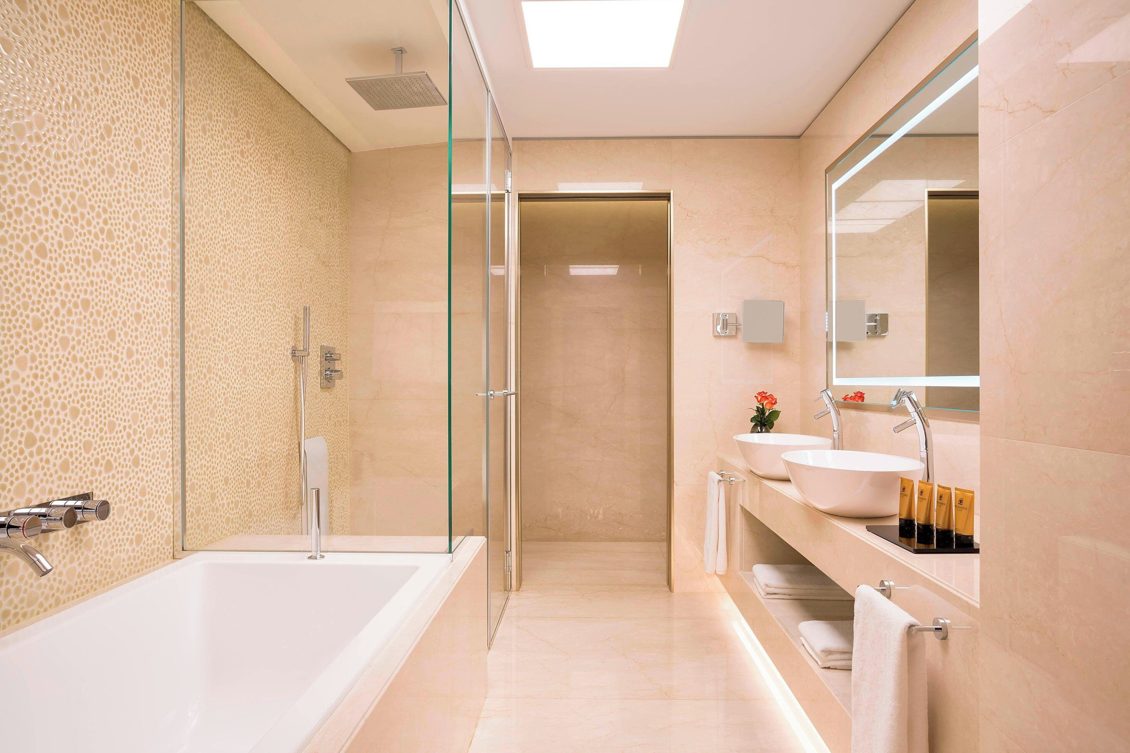 Een moderne badkamer met een glazen douchecabine, een ruim bad en een wastafel met twee wasbakken.