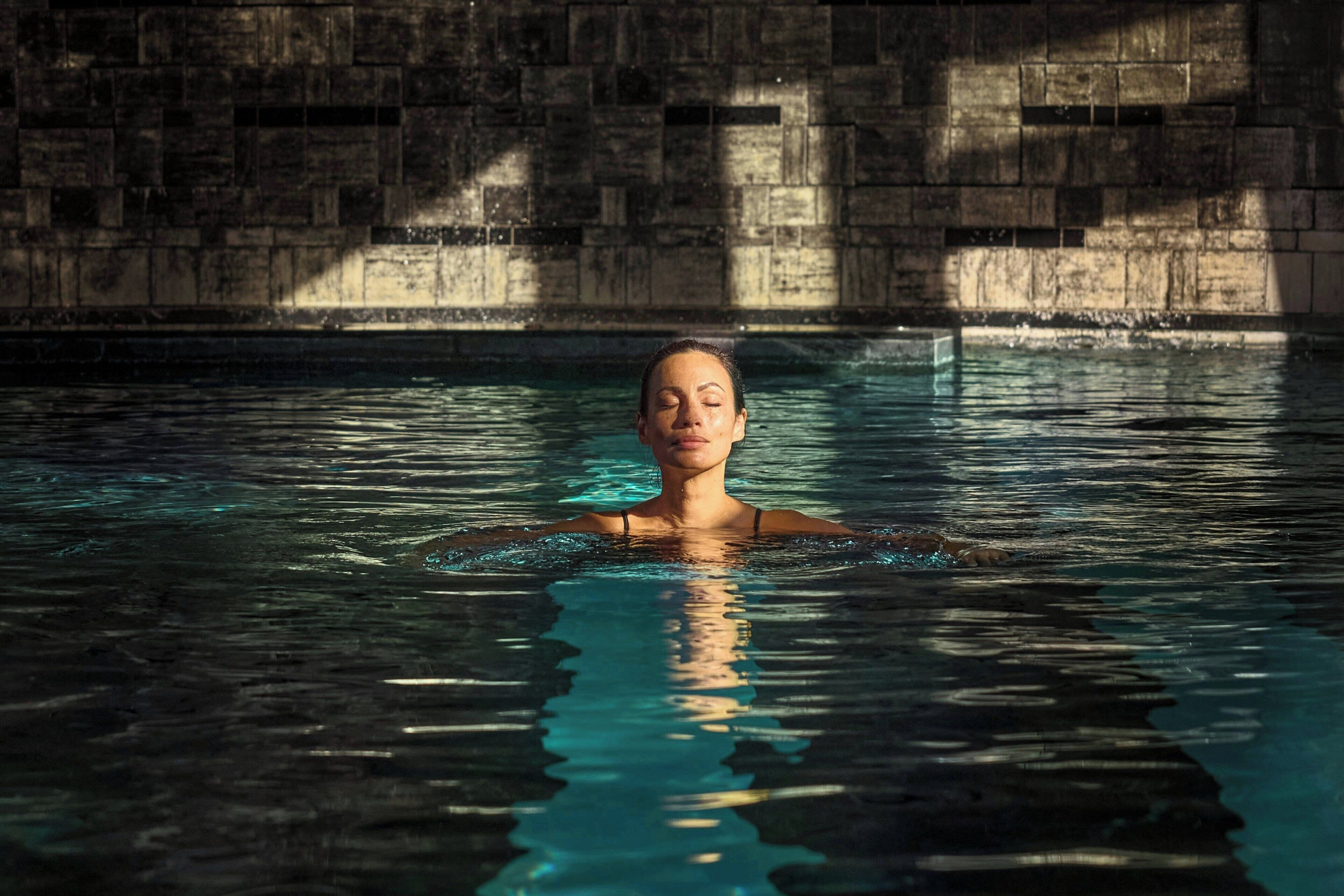 Una persona nada en una piscina con un muro de piedra al fondo.