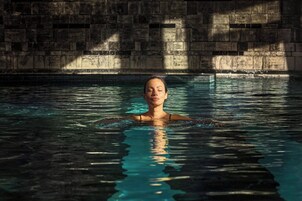 Una persona nuota in una piscina con un muro di pietra sullo sfondo.