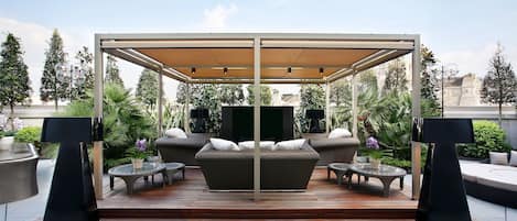 A covered outdoor seating area with a sofa, two tables, and a TV.