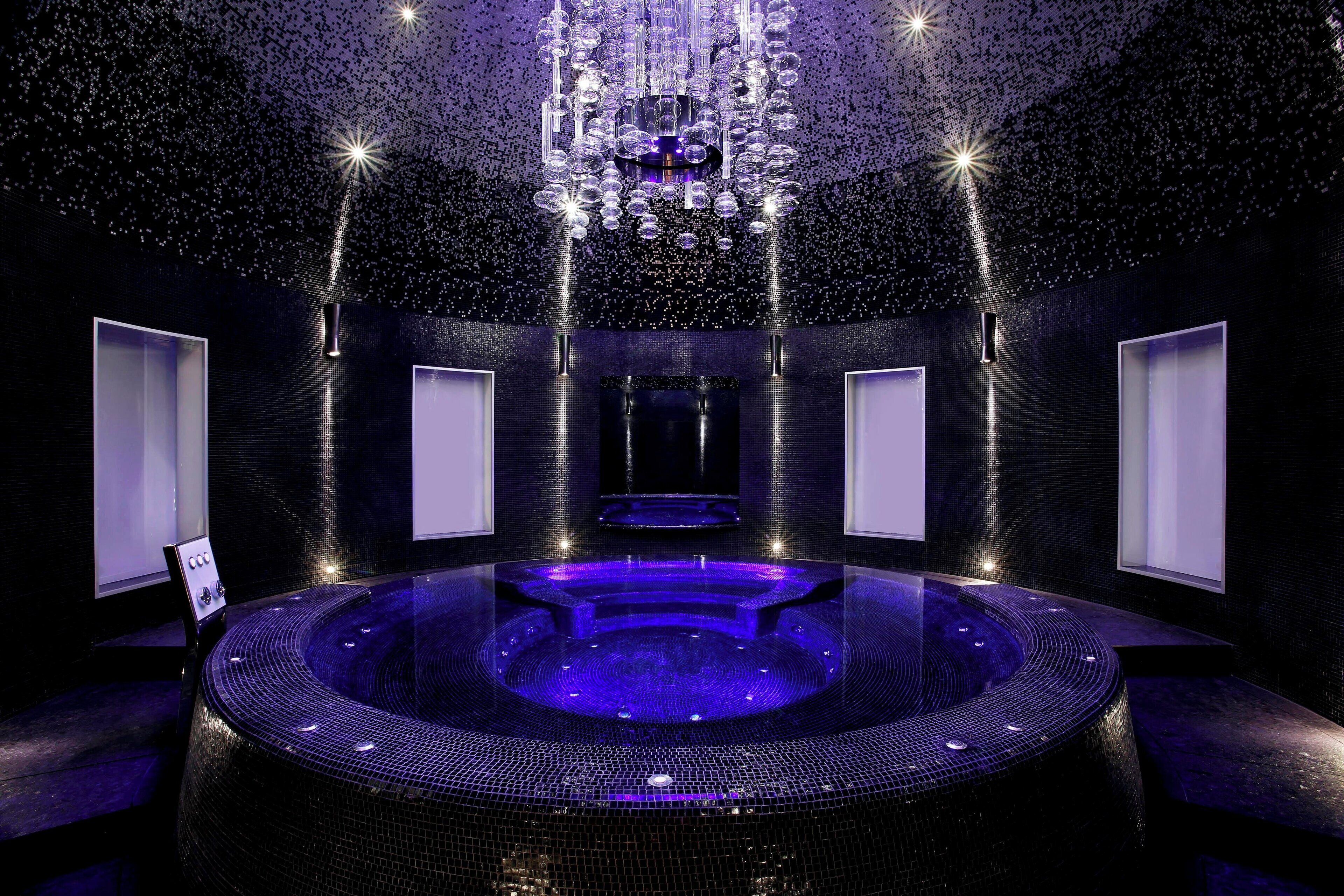 Un spa moderno con una bañera de hidromasaje circular, una araña y una pared oscura con textura.