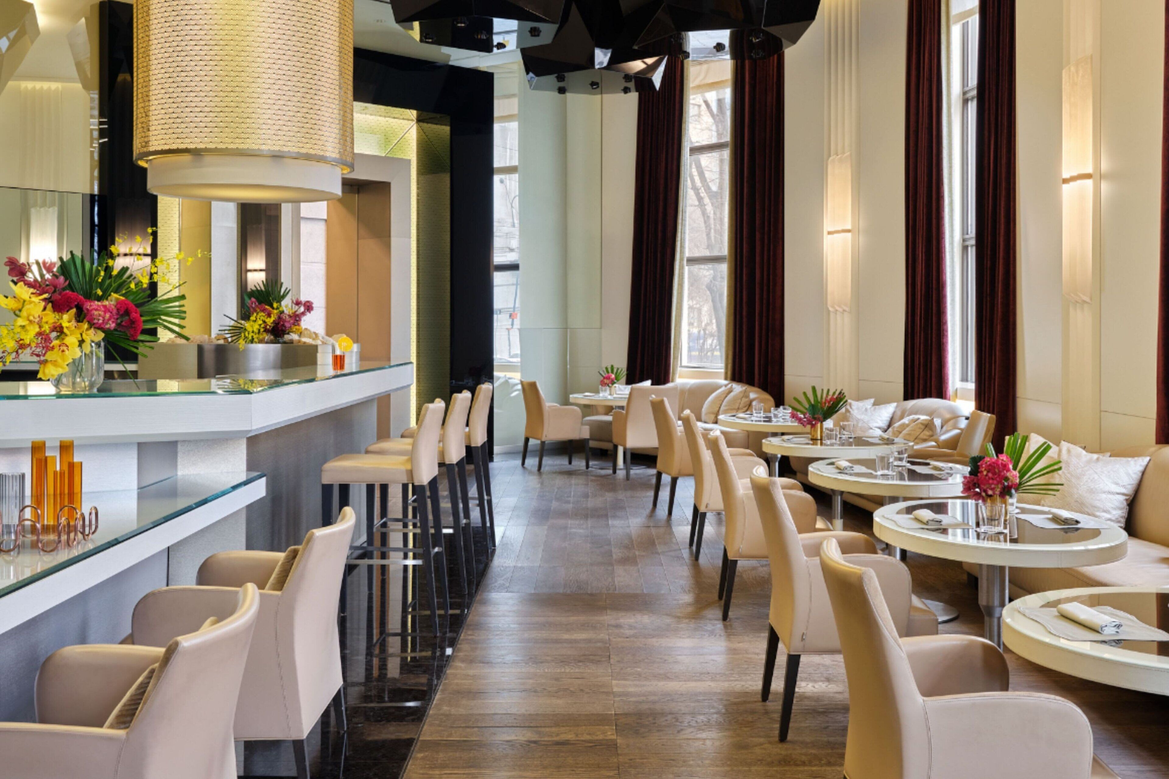 Un restaurant moderne doté d’un bar, de plusieurs types de tables, notamment des tables rondes et des tabourets de bar, et d’une allée centrale.