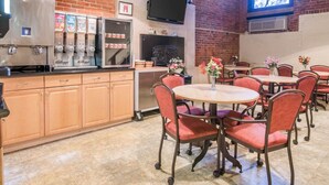 A restaurant with brick walls, a coffee machine, a TV, and red chairs. - Econo Lodge Manchester (Manchester)