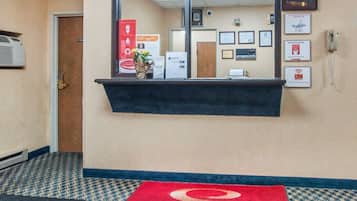 Ein Hotel-Empfangsbereich mit einer Rezeption, gerahmten Zertifikaten und einem roten Teppich mit dem Namen des Hotels.