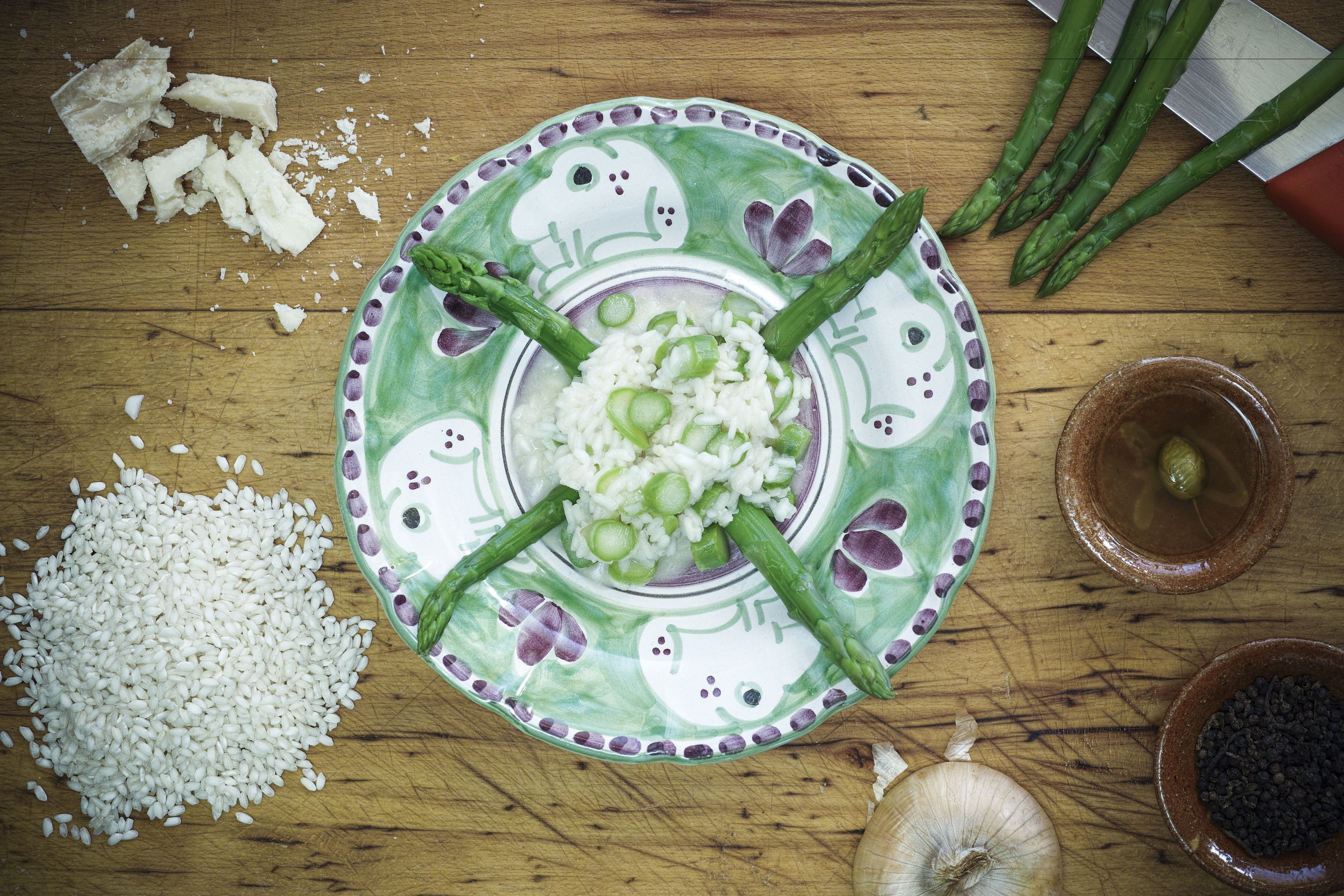 A plate of rice with asparagus, a bowl of black pepper, and a whole onion on a wooden table.