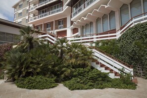 Un hotel de varios pisos con una escalera central, rodeado de exuberante vegetación y palmeras.