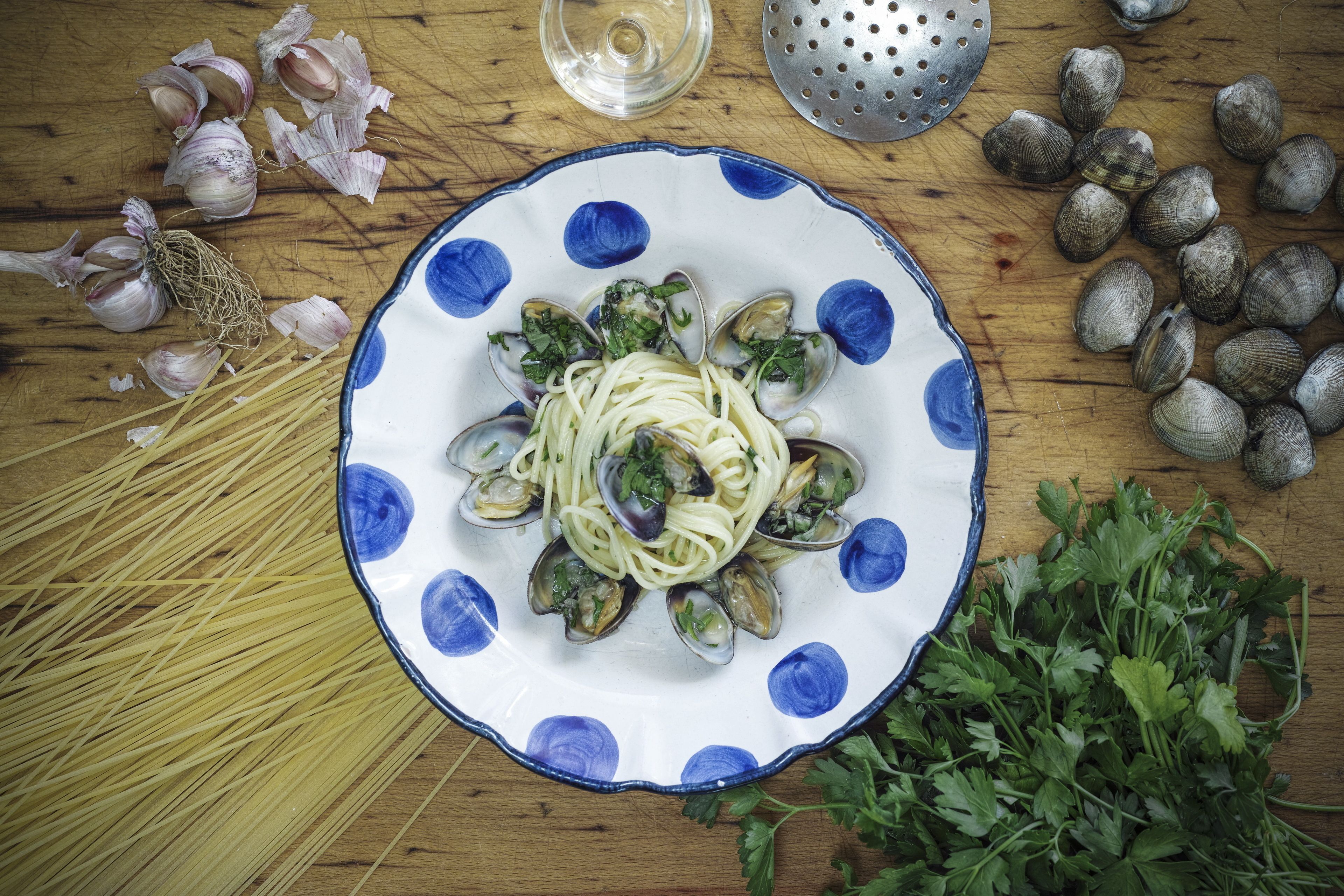 A plate of pasta with clams and herbs, garlic, and parsley on a wooden table.