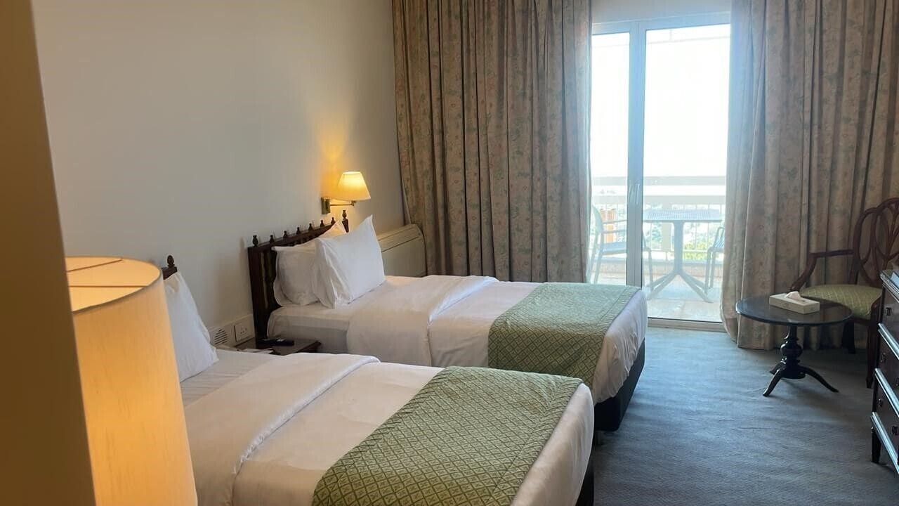 Habitación de hotel con dos camas, un escritorio, una silla y vistas al exterior.