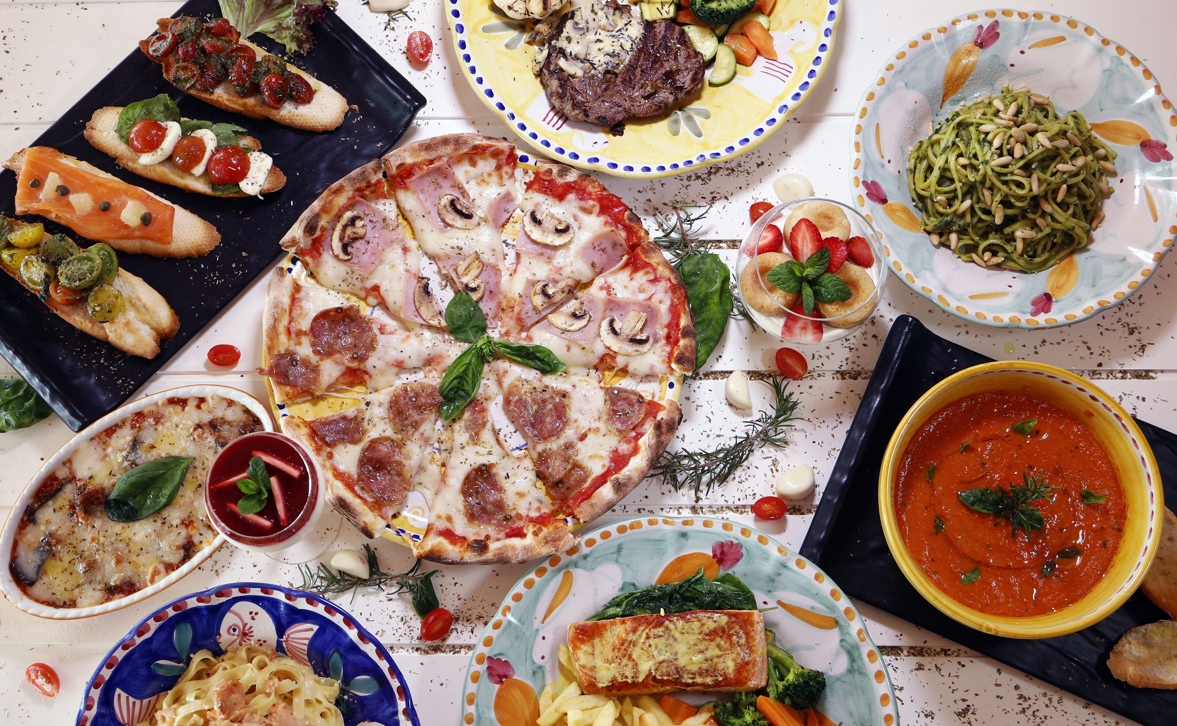 Diversos plats, com pizza, pasta i un bol de sopa, disposats sobre una taula.