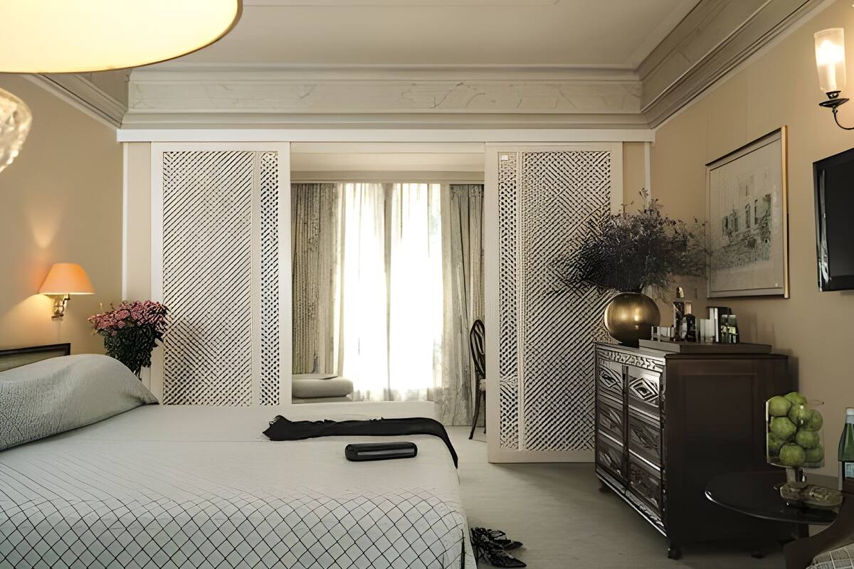 Une chambre d’hôtel avec un lit, une commode, une lampe, un téléviseur et une vue sur l’extérieur, visible à travers une porte.