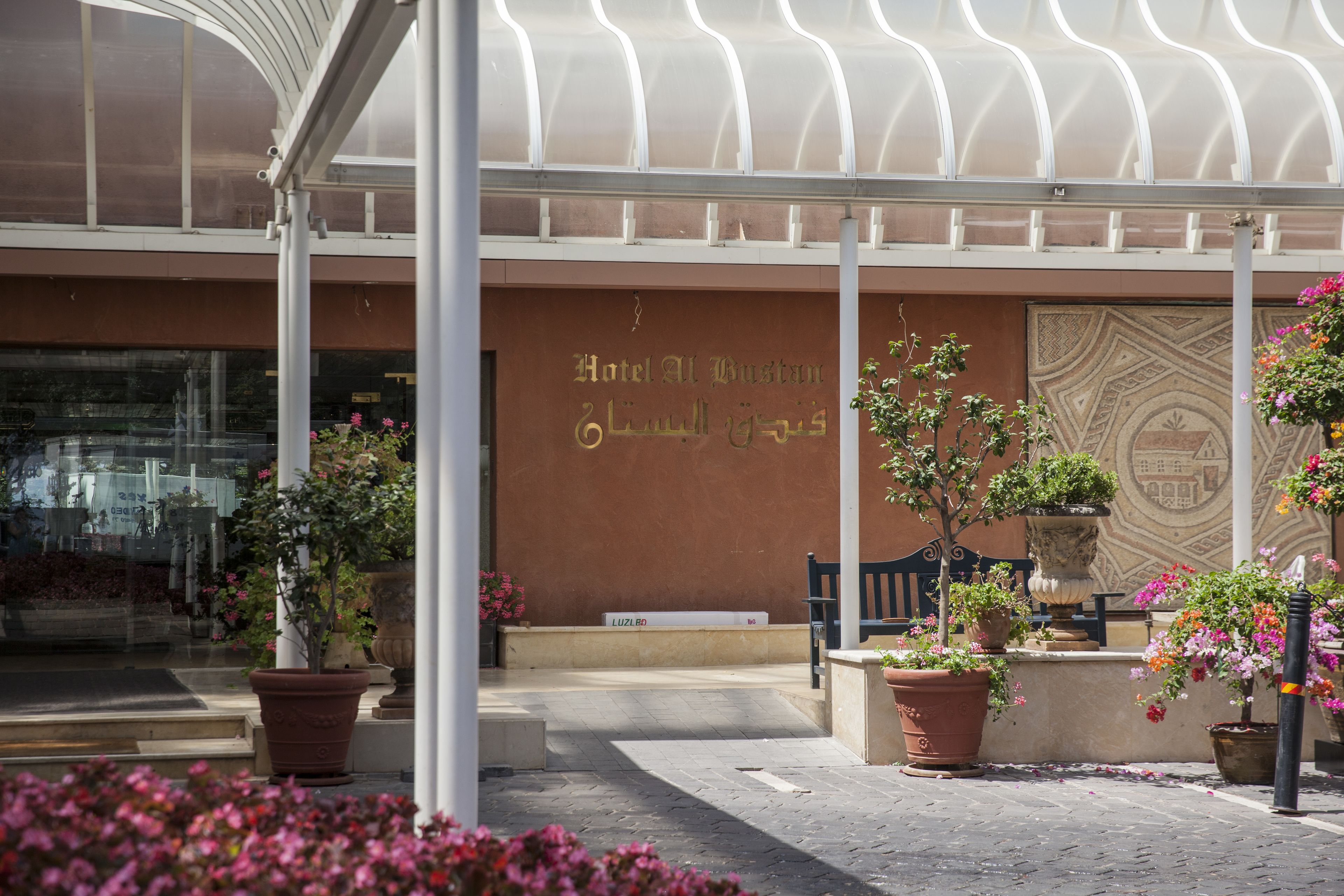 A hotel entrance with a covered patio area, potted plants, and a bench.