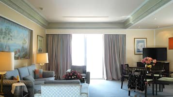 Une chambre d’hôtel avec un canapé, des fauteuils, une table à manger, un téléviseur et un tableau au mur.