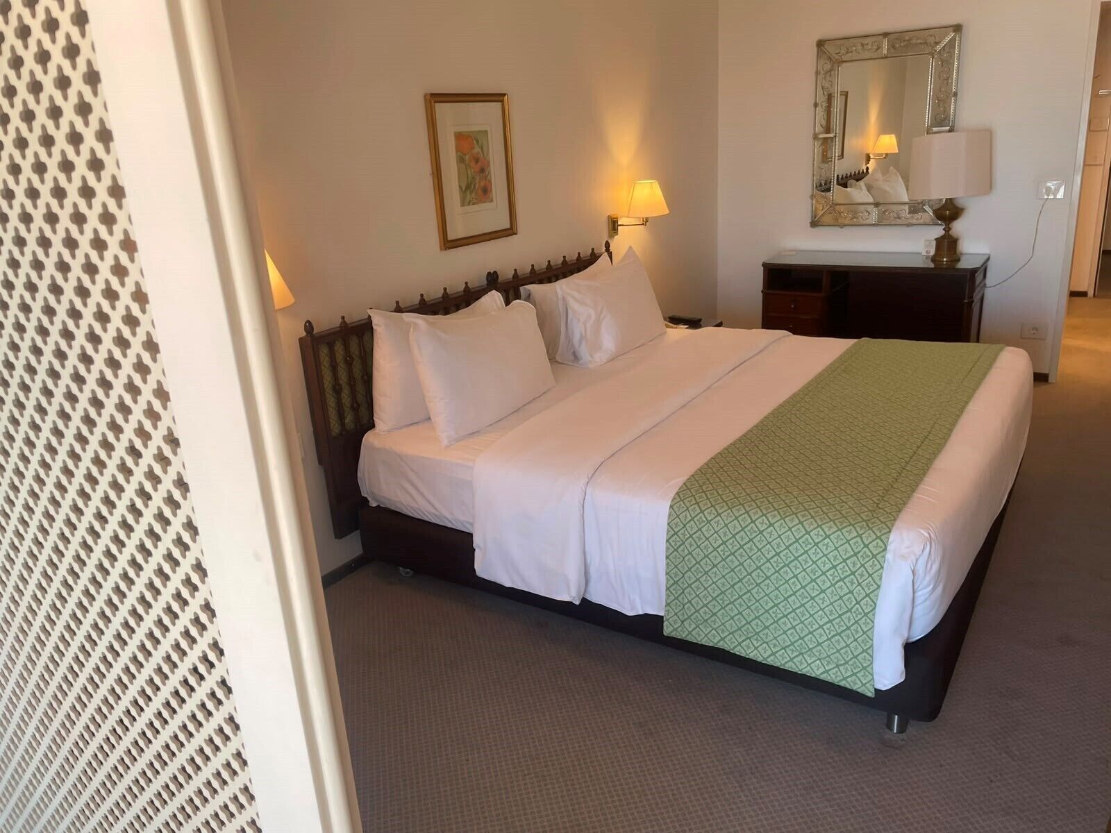 A hotel room with a bed, a dresser, a mirror, and a wall-mounted picture.