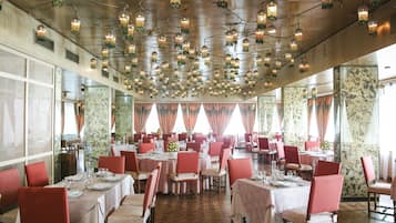 Un restaurante con varias mesas dispuestas para comer, que cuenta con un techo alto con luces colgantes y un muro con diseño.