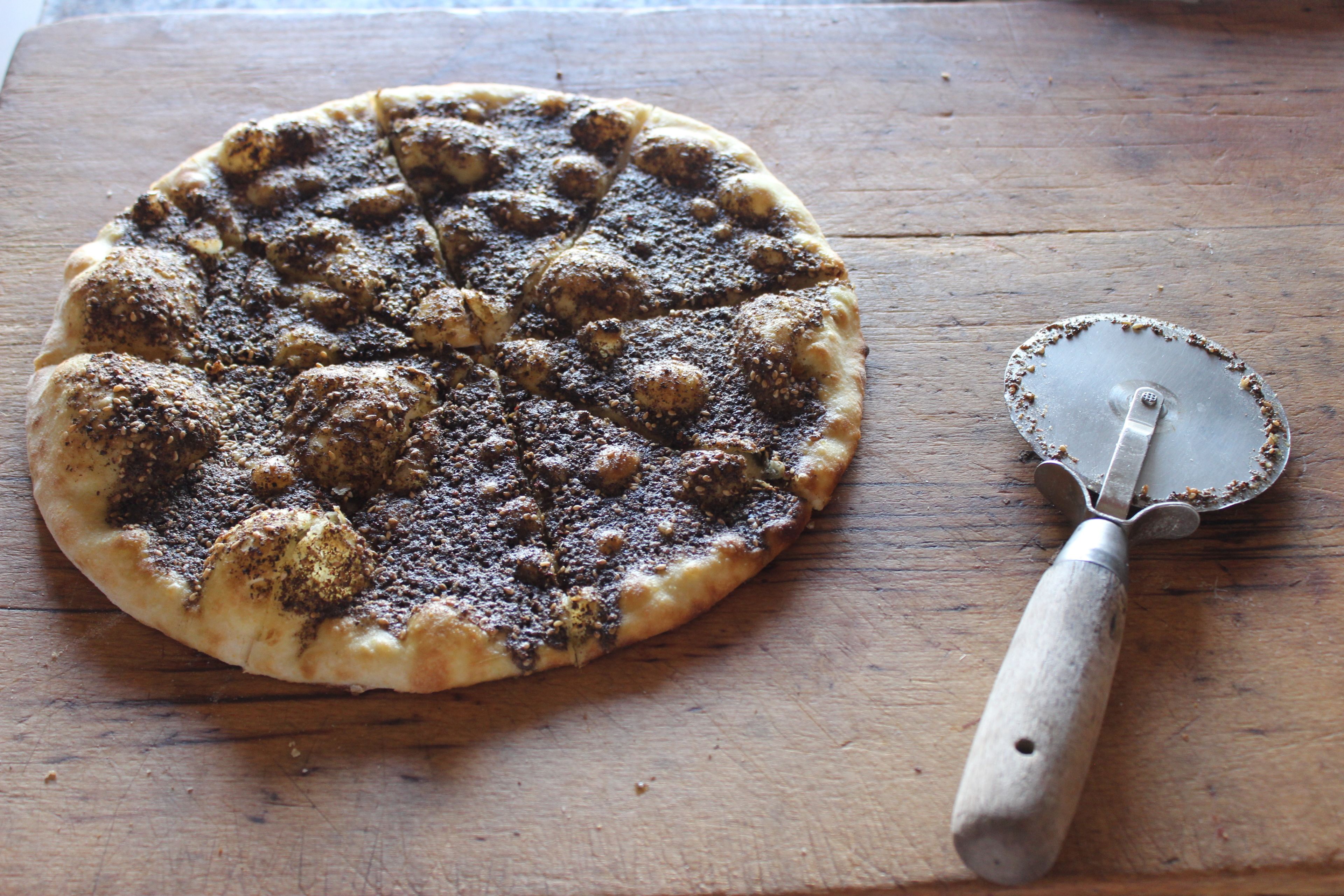 Una pizza sobre una tabla de madera con un cortador de pizza a su lado.