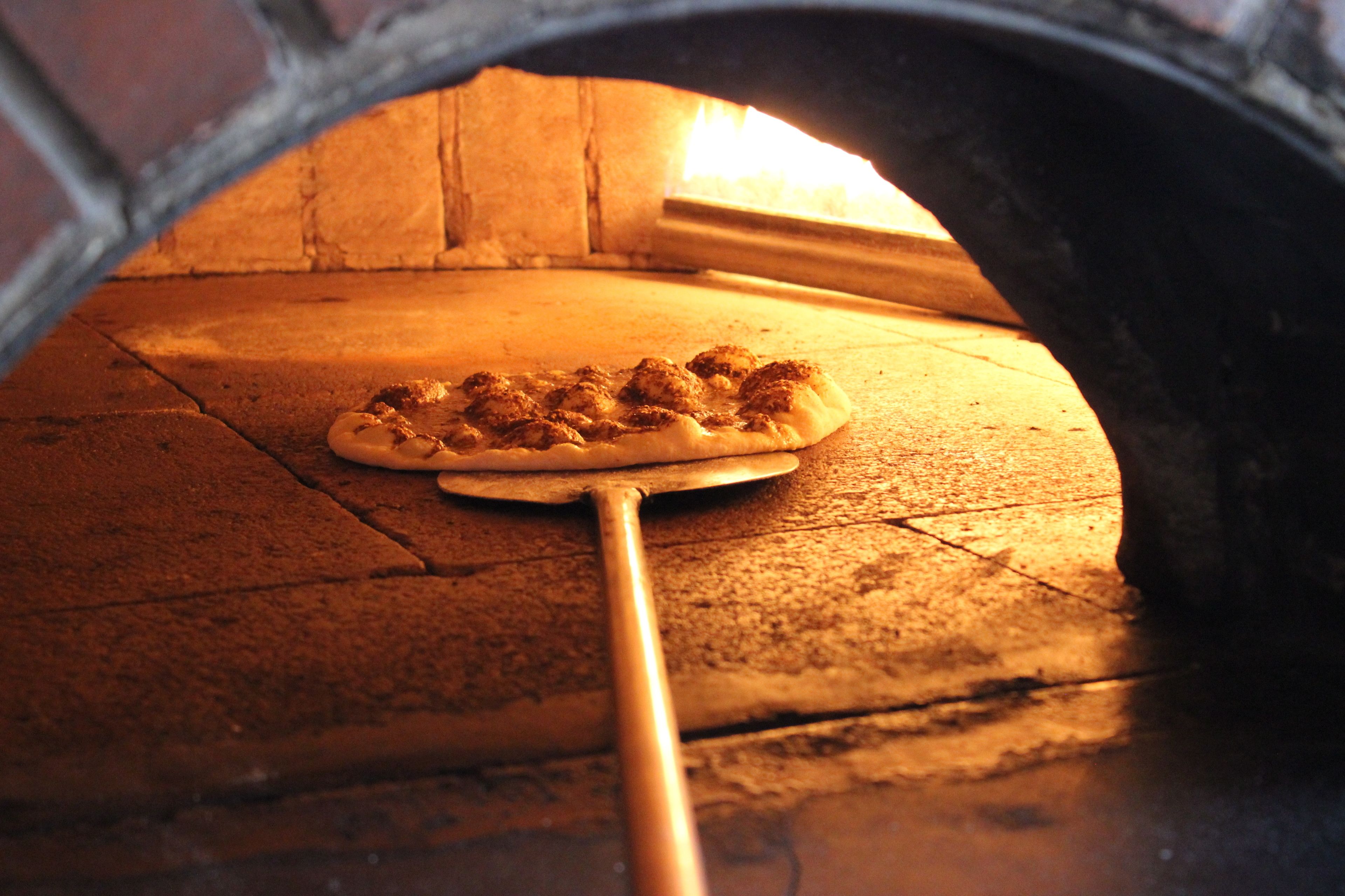 Una pizza in un forno in mattoni con una pala di legno.