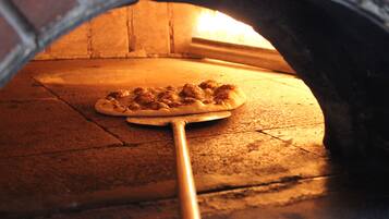 Una pizza in un forno in mattoni con una pala di legno.