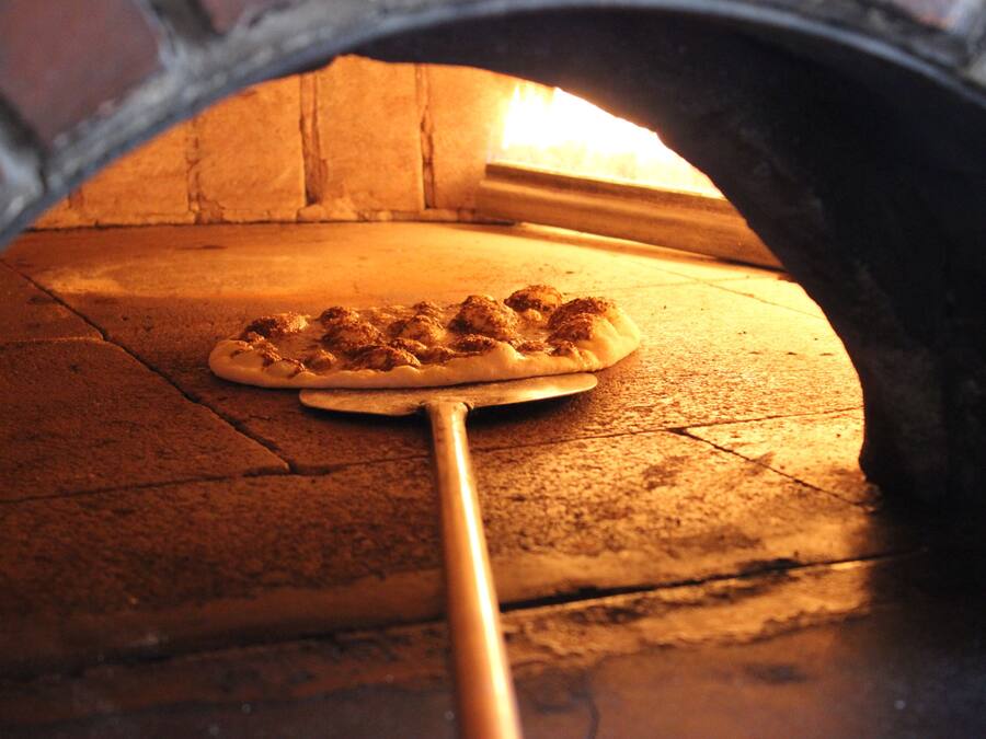 A pizza inside a brick oven with a wooden peel.