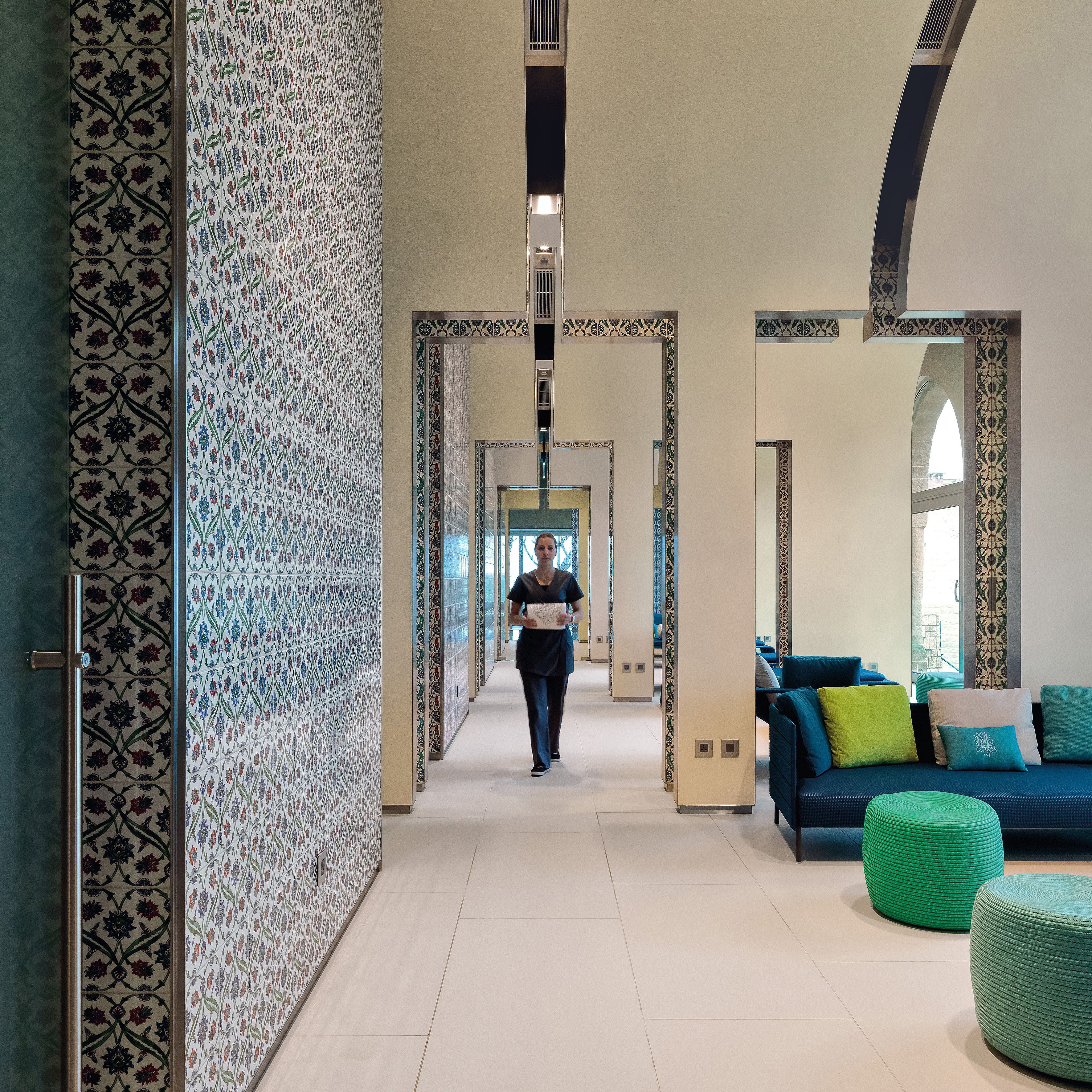 A hallway with patterned walls, a blue sofa with cushions, and a person walking.