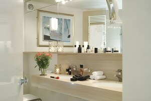 Un baño moderno con un espejo grande, un cuadro abstracto enmarco, un florero con flores y artículos de tocador sobre la encimera.