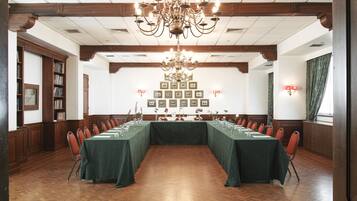 A conference room with a long table, chairs, a chandelier, framed pictures on the wall, and wooden paneling.