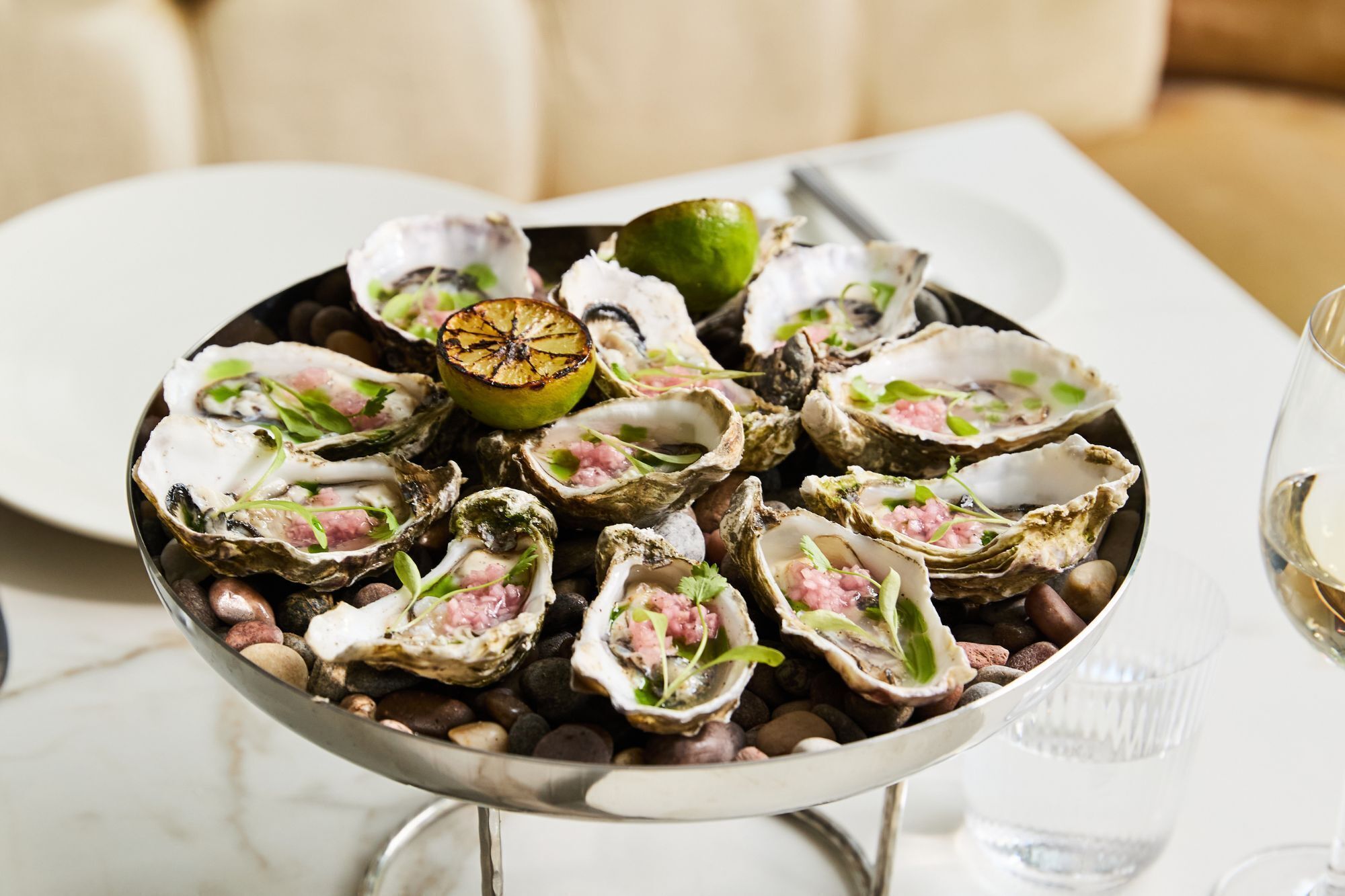 Een schaal oesters, gegarneerd met limoen en peterselie, gepresenteerd op een laagje kleine ronde stenen.