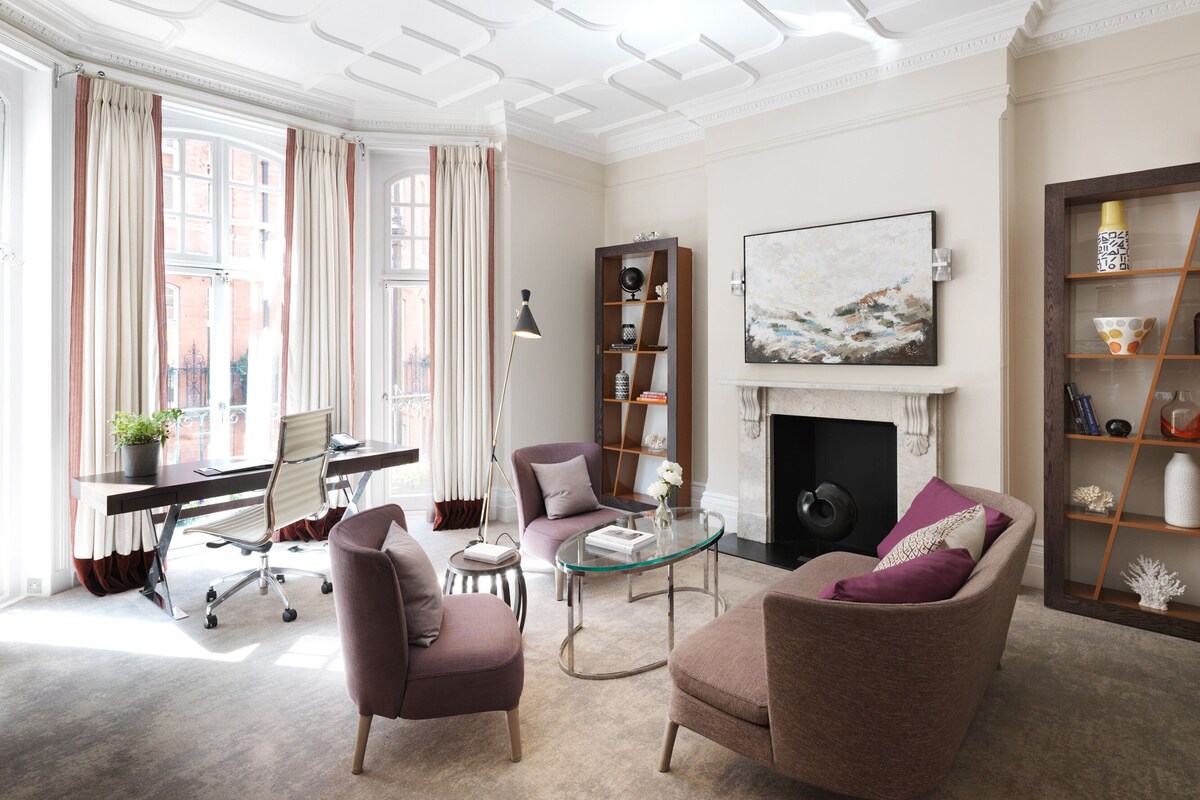 A well-lit living room with a fireplace, a bookshelf, and a comfortable seating area.