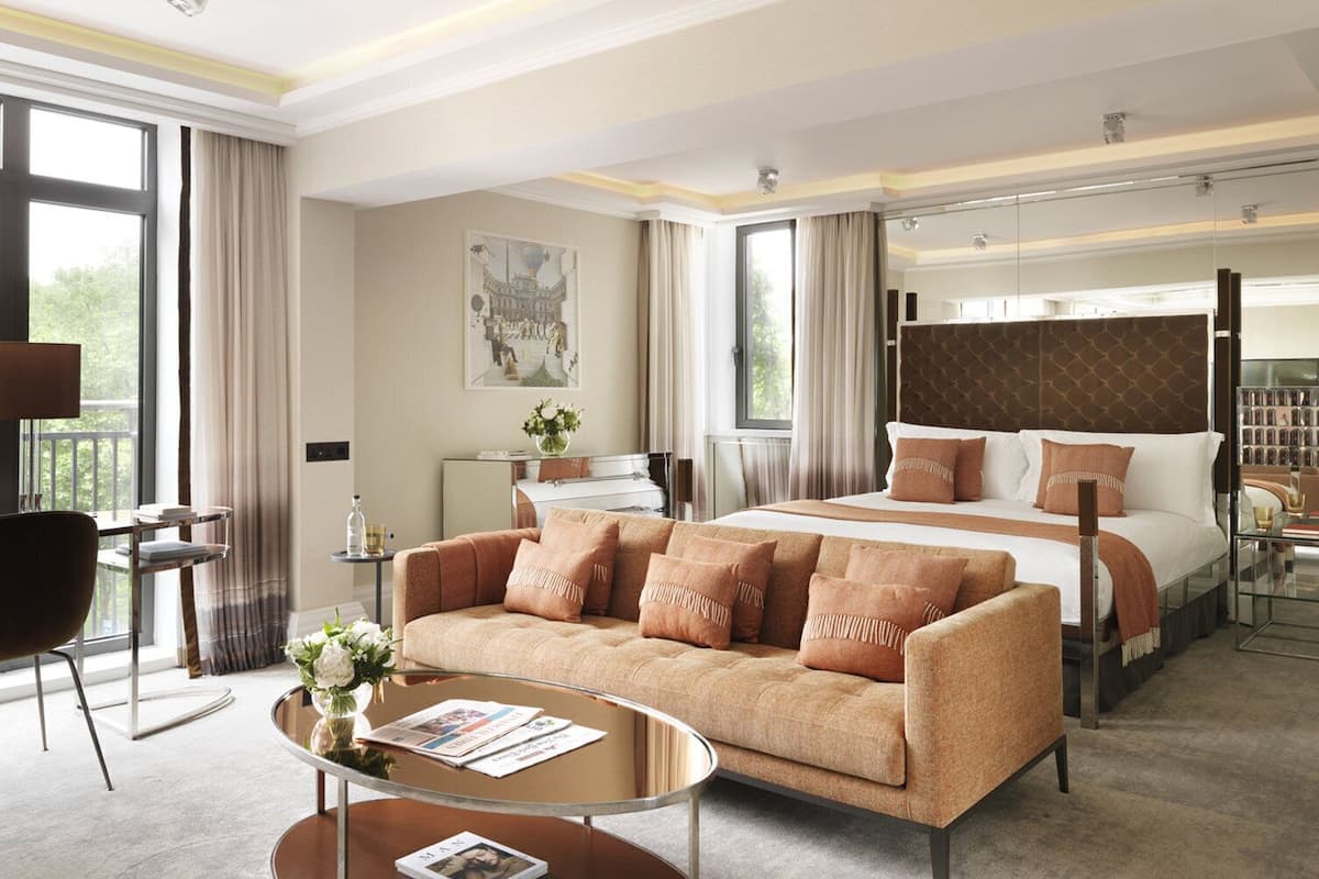 A hotel room with a bed, a sofa, a coffee table, a desk, and a large window.