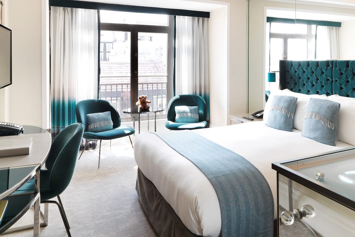 A hotel room with a large bed, two chairs, a small table, a desk with a keyboard, and a large mirror.
