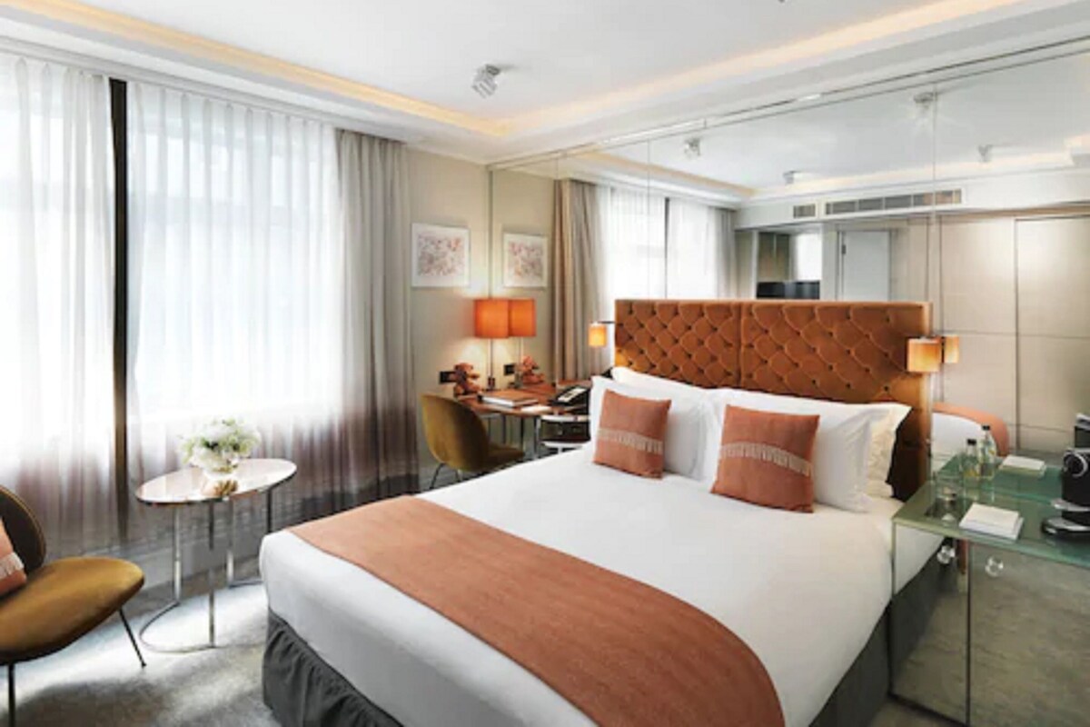 A hotel room with a large bed, a desk, a chair, and a small table.