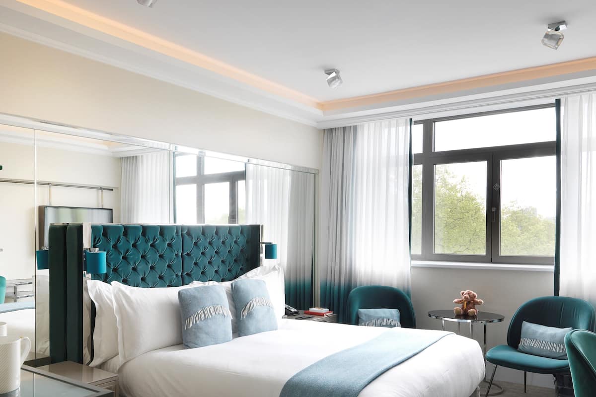 A modern hotel room with a large bed, a desk, a chair, and a window with curtains.