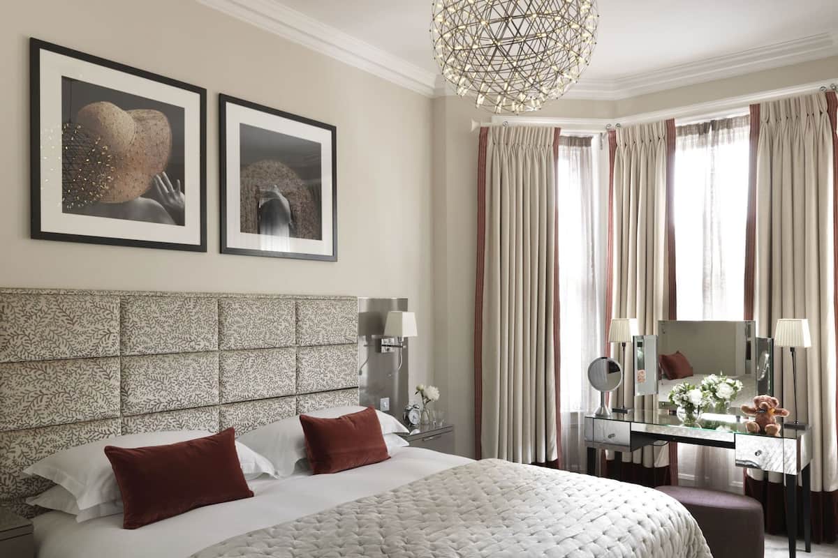 A hotel room with a large bed, a desk, a chair, a mirror, and two framed pictures on the wall.