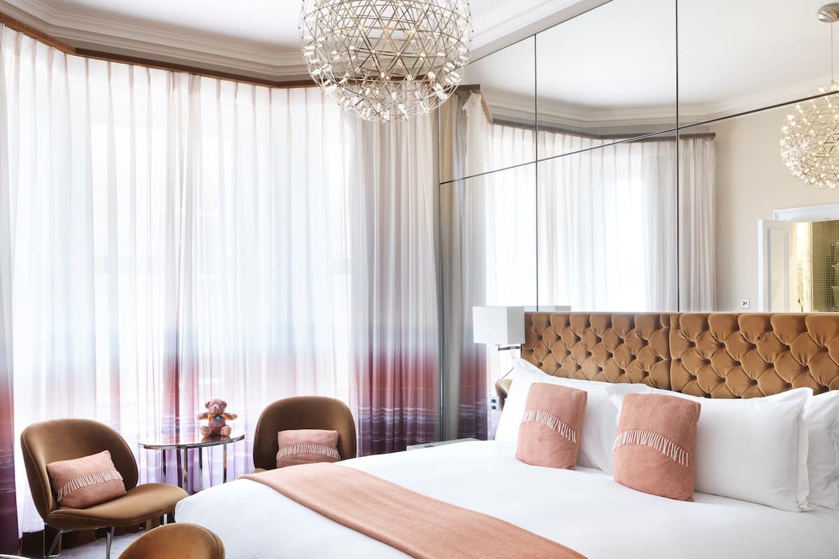 A hotel room with a large bed, two chairs, a small table, and a chandelier.