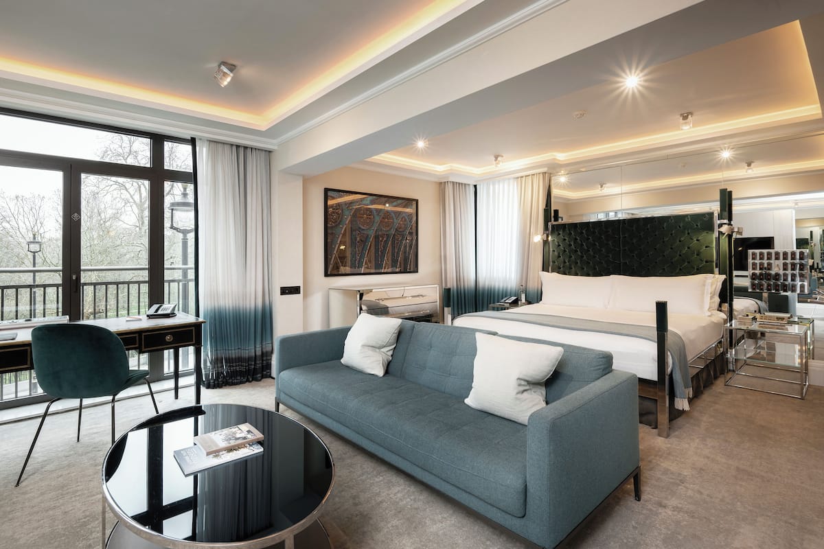 A modern hotel room with a large bed, a sofa, a desk, and a view of the outdoors.