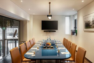 A conference room with a long table, chairs, a television, and a window with a view.
