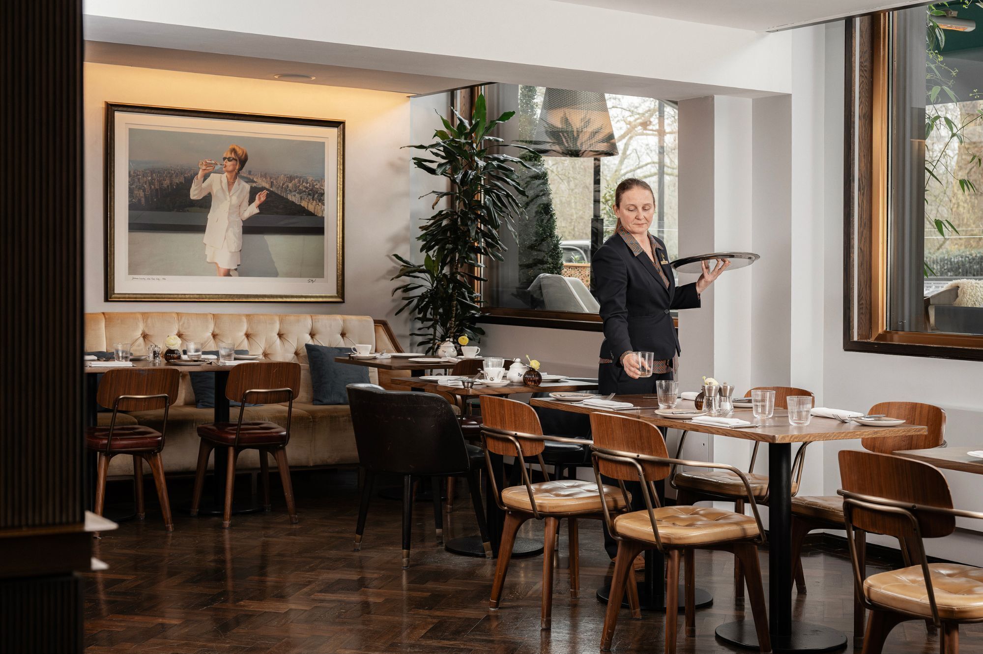 Ein Restaurant mit Holztischen, einem großen Bilderrahmen an der Wand und Blick ins Freie durch große Fenster.