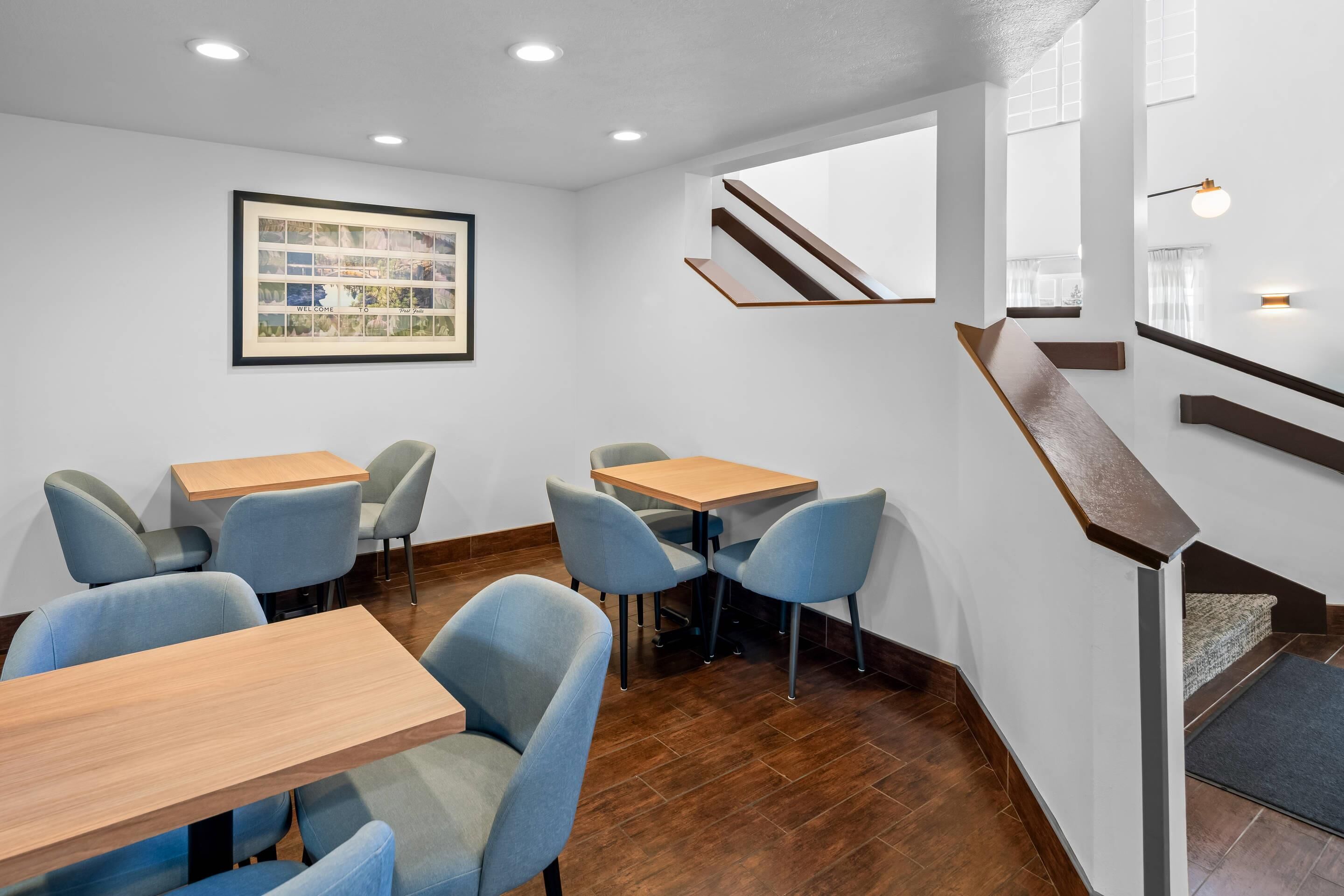 Un interior moderno con mesas y sillas de madera, un letrero de bienvenida enmarco y una escalera.