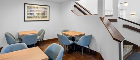 Un interior moderno con mesas y sillas de madera, un letrero de bienvenida enmarco y una escalera.
